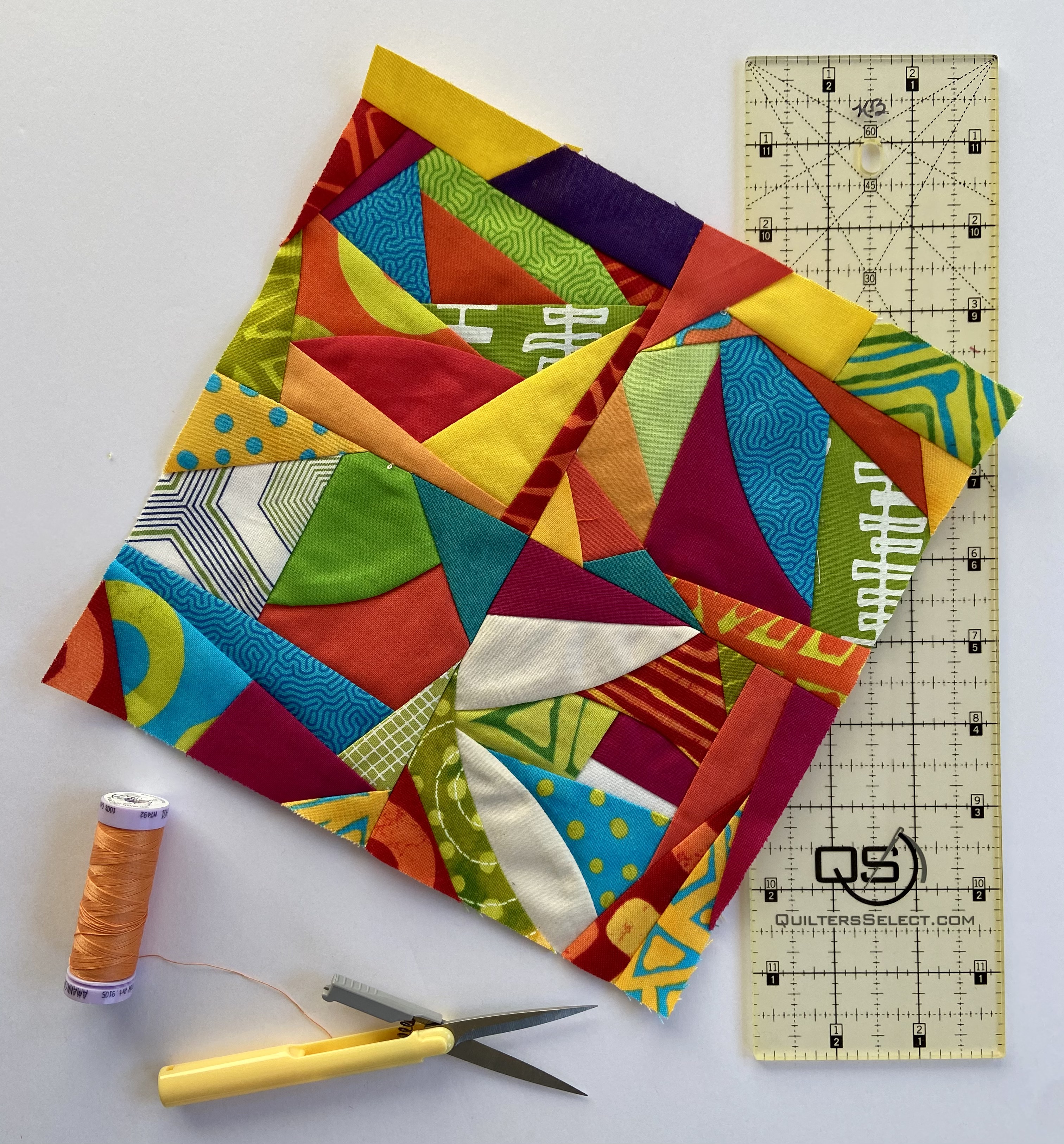 Cazy quilt block made of small scraps, with spool of thread, thread nippers, and rotary ruler.
