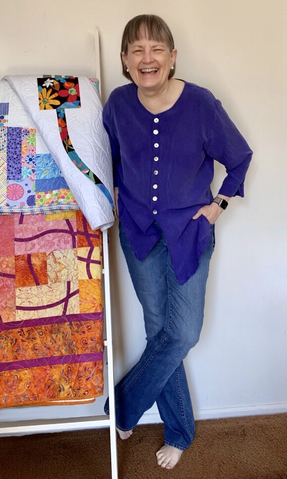 Photo of woman standing next to quilt ladder, with 3 quilts